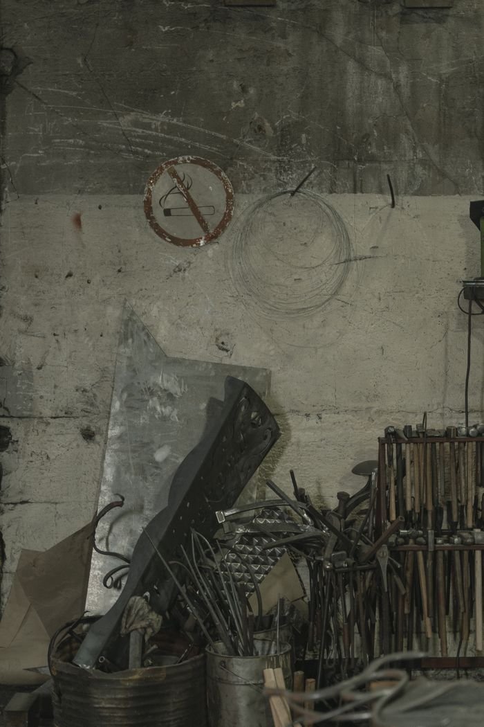 A collection of metal scraps, tools, and steel components in a dimly lit warehouse corner.